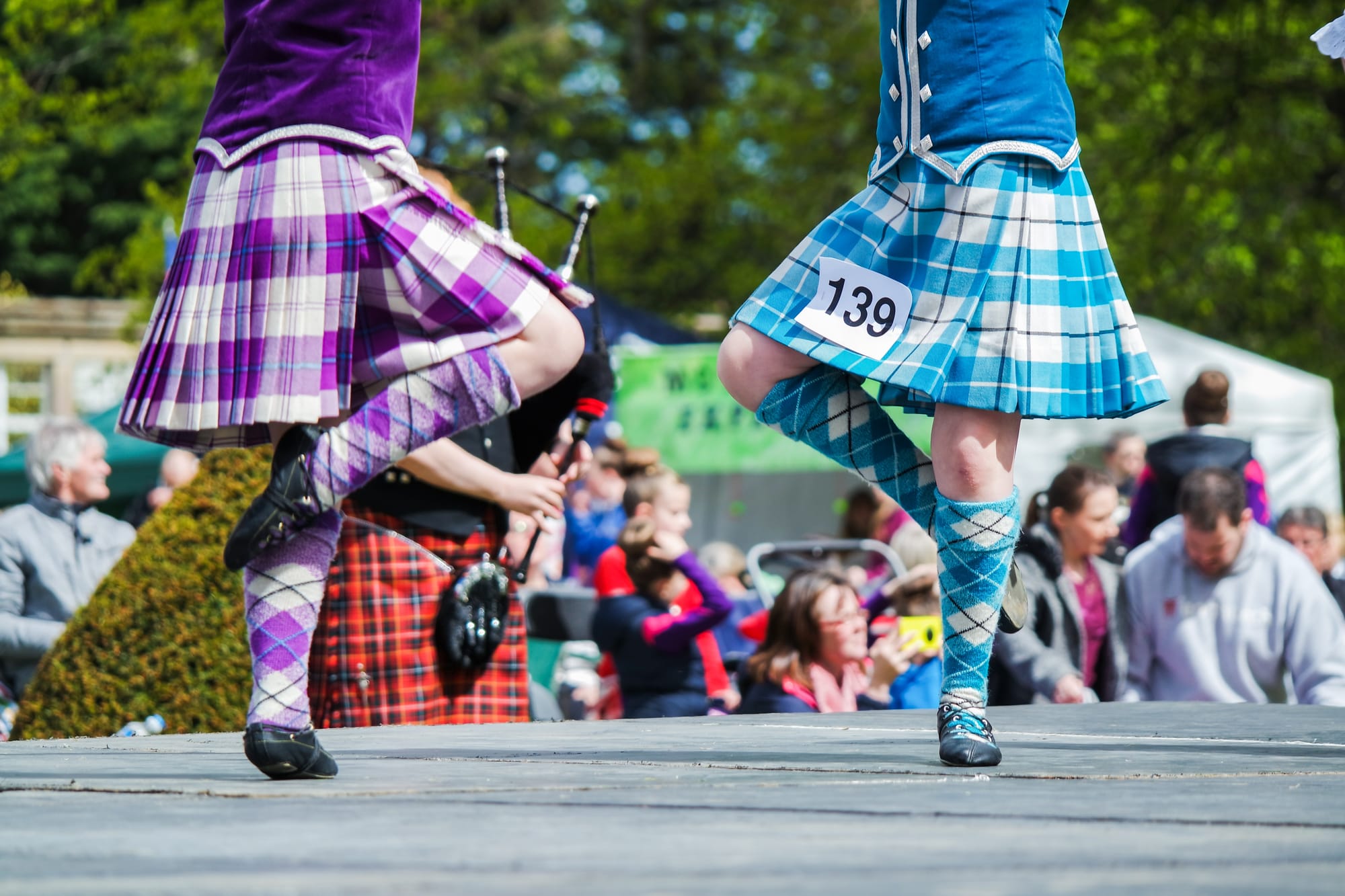 Two girls dance on a stage in kilts with a competitor number visible.