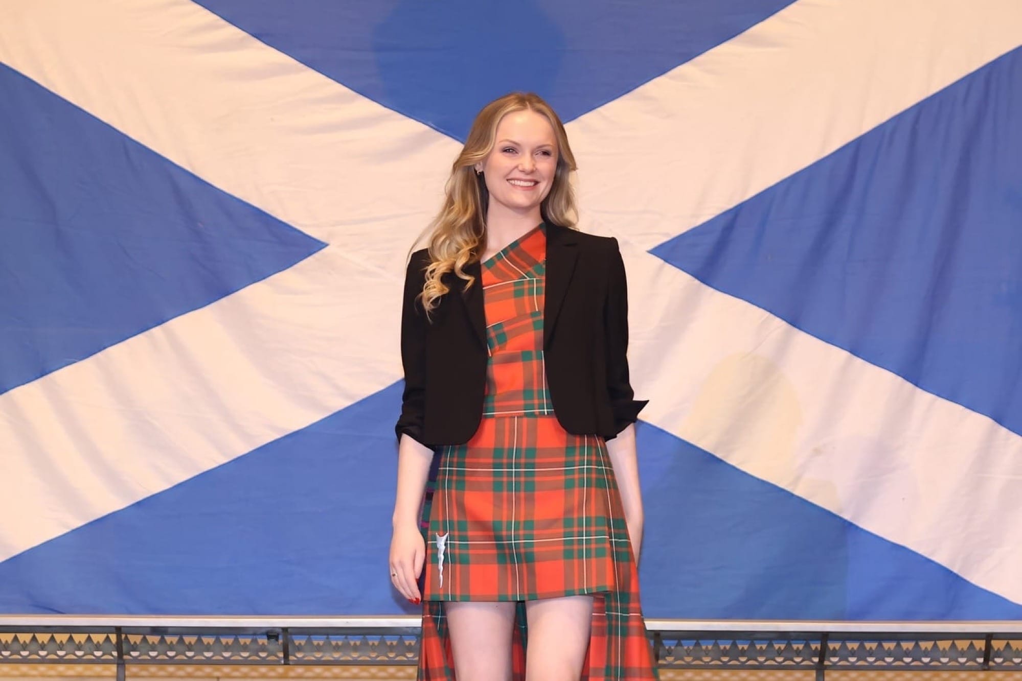 Iona MacGowan in a tartan dress in front of a Saltire flag.