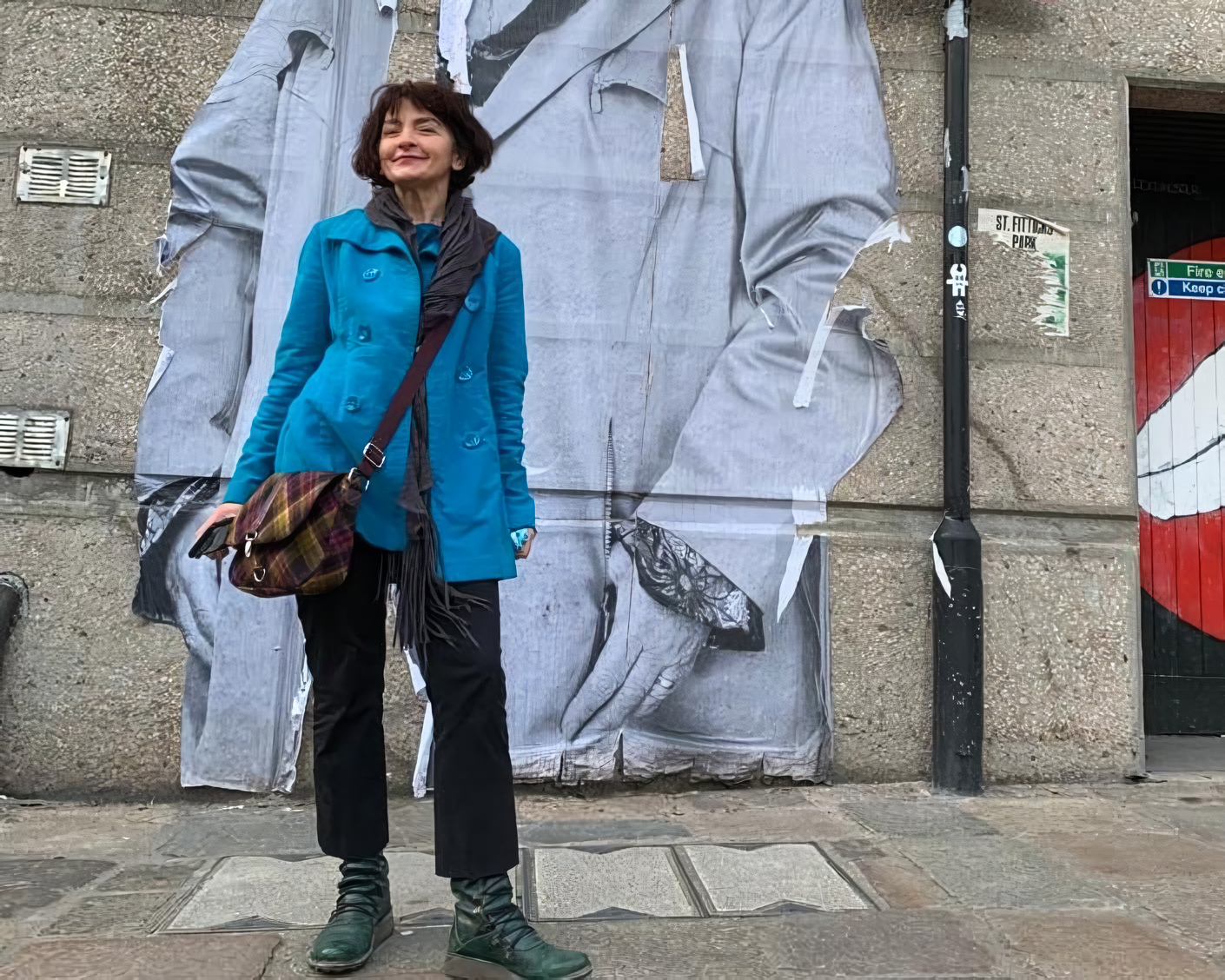 Morag standing on a pavement wearing a blue coat and a tartan bag.