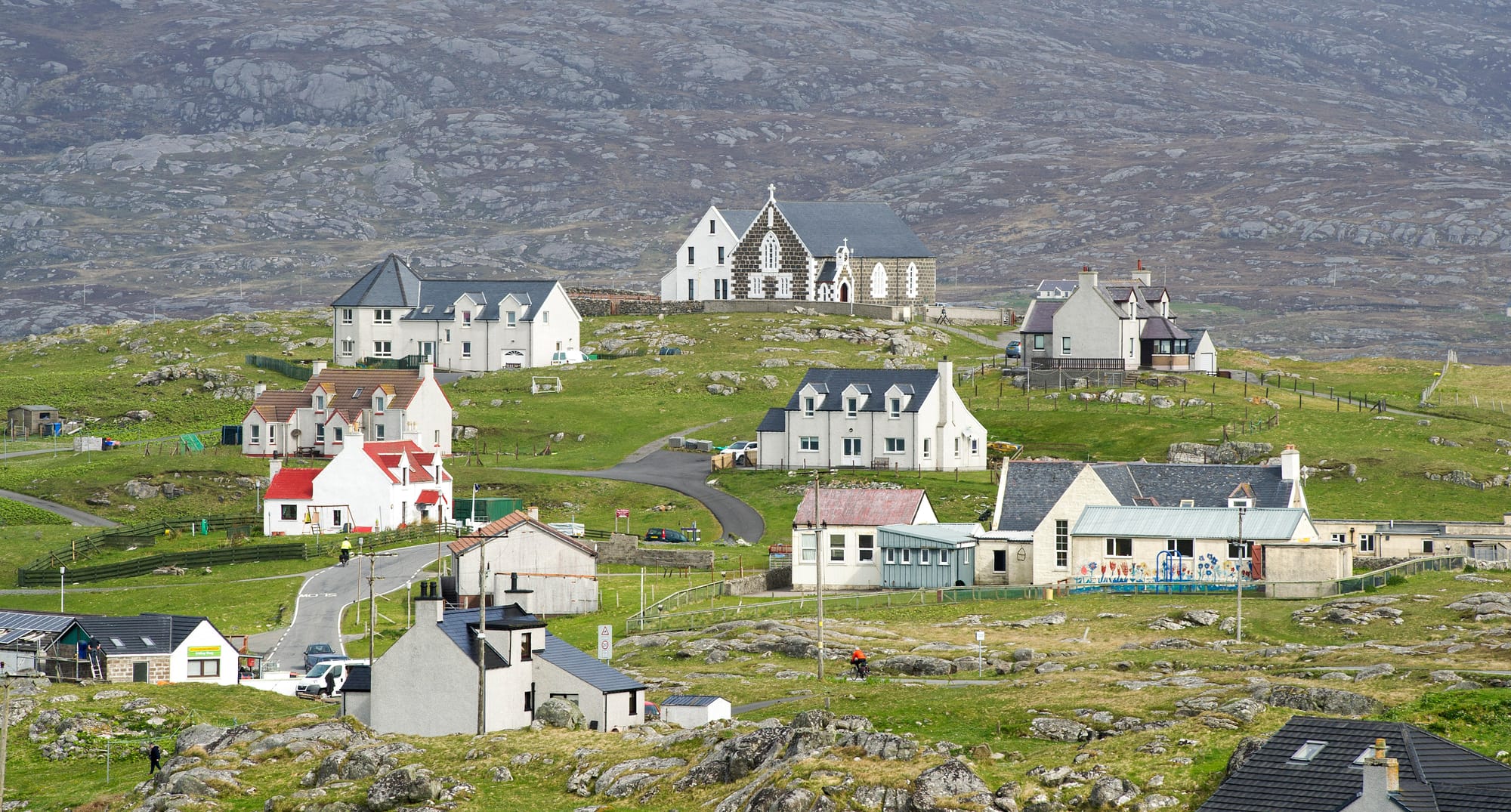 Several houses on a rocky hillside on Eriskay - the stone church of St Michaels sits at the top of the hill.