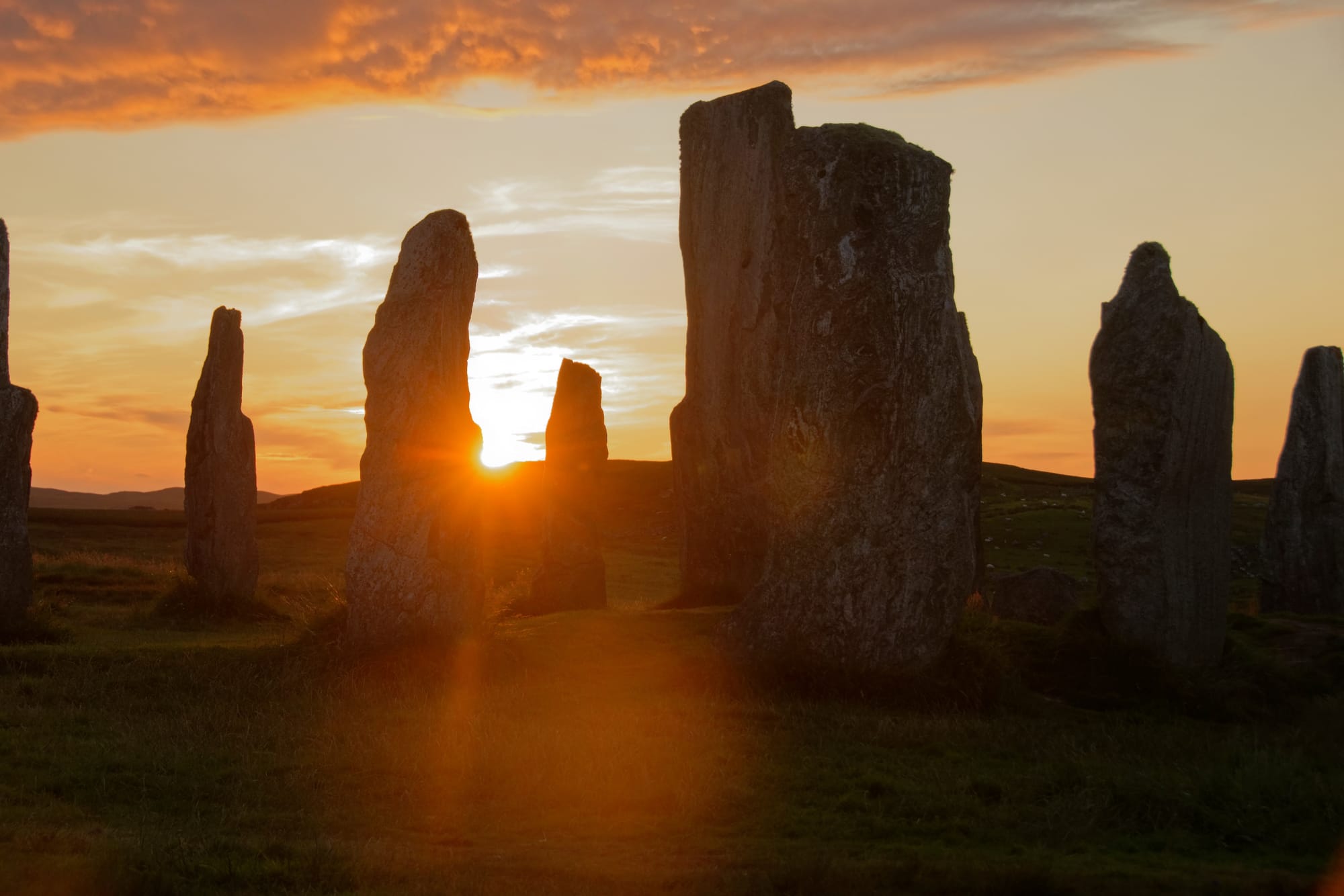 The outlines of the Calanais Standing stones with a bright sunset behind them.