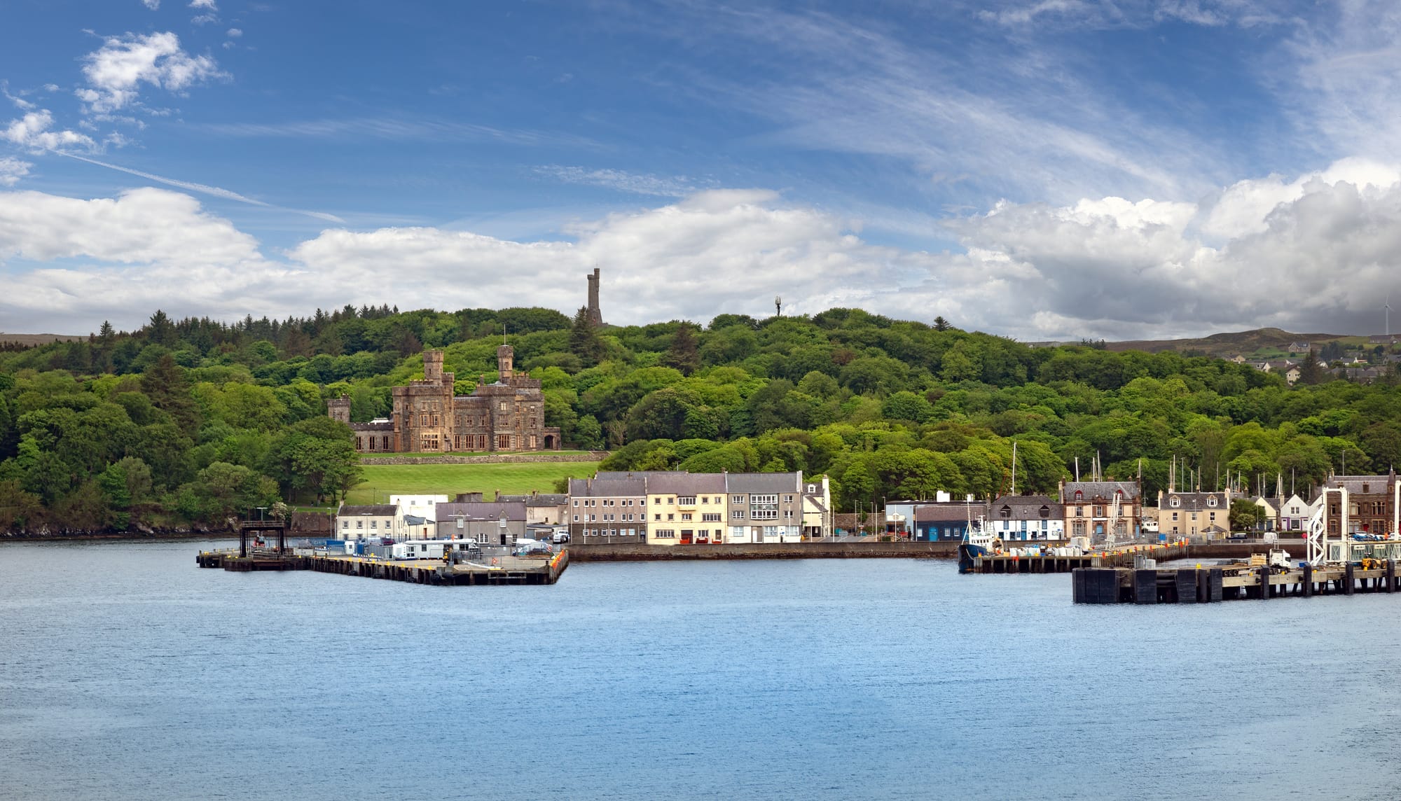 The harbour at Stornoway on Lewis - a row of houses with the Castle of The Earl of Lewis and a wooded hill behind them.