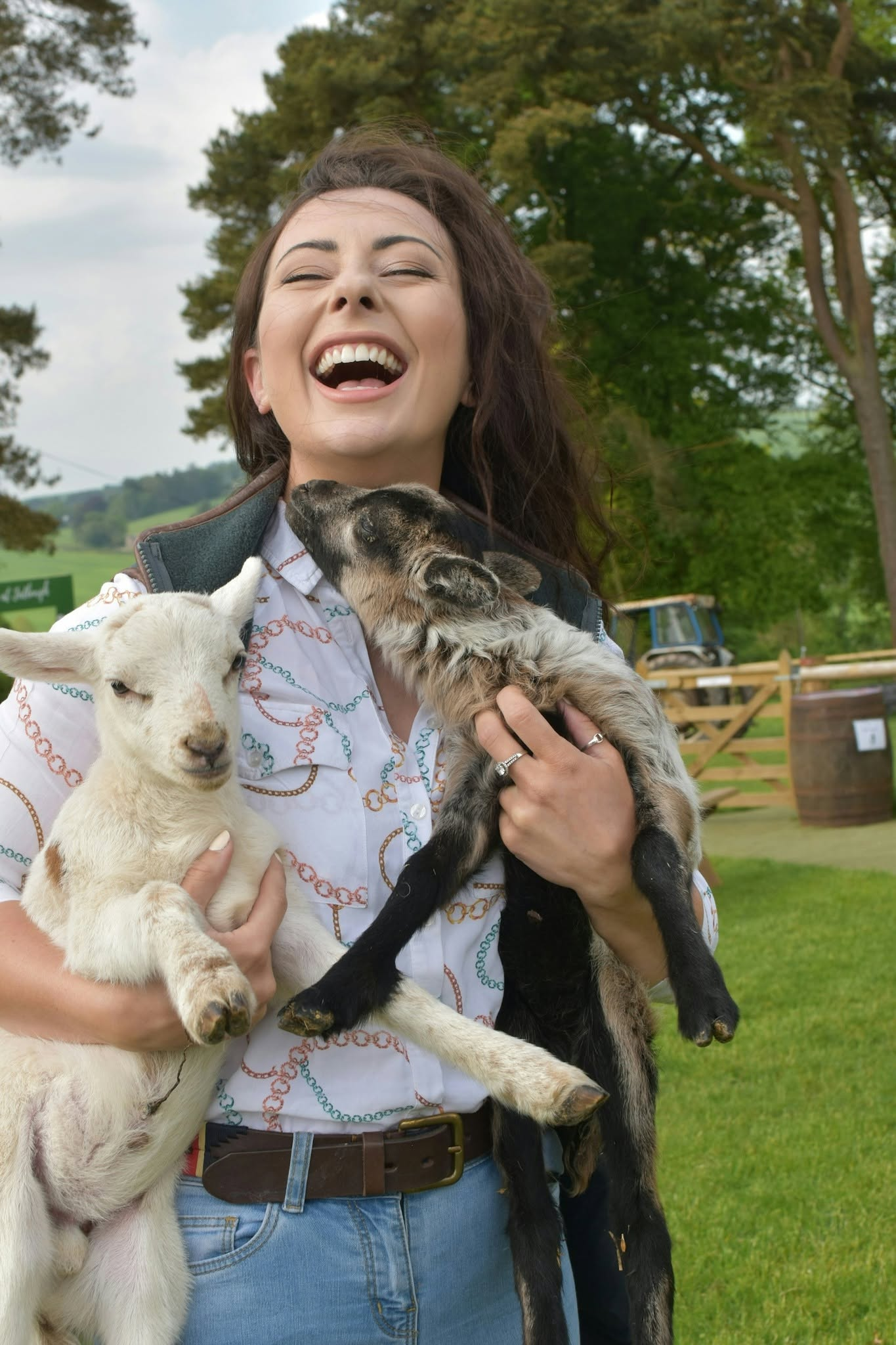 A laughing woman cuddles two young lambs, one white and one grey at Jacksons at Jedburgh