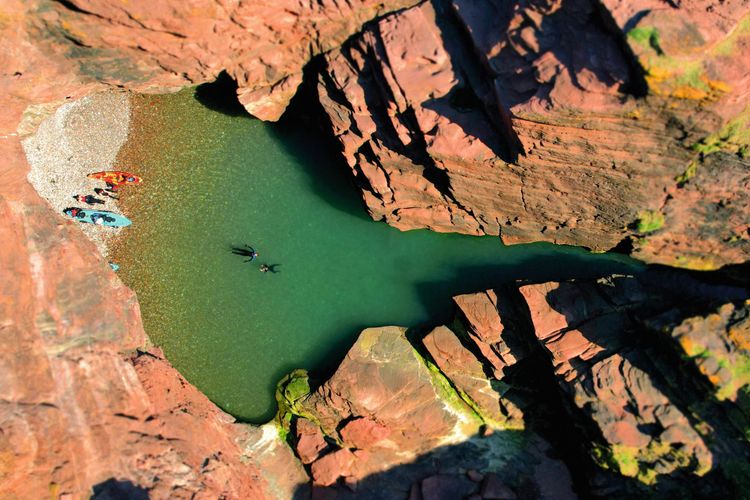 Aerial view of a small beach and green water between red sandstone cliffs.