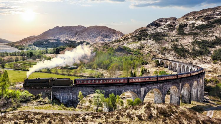 An aerial view of a steam train crossing the Glenfinnan Viaduct.