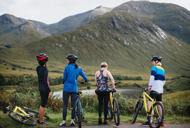 A group of four cyclists take a break looking over water towards greemountains. 