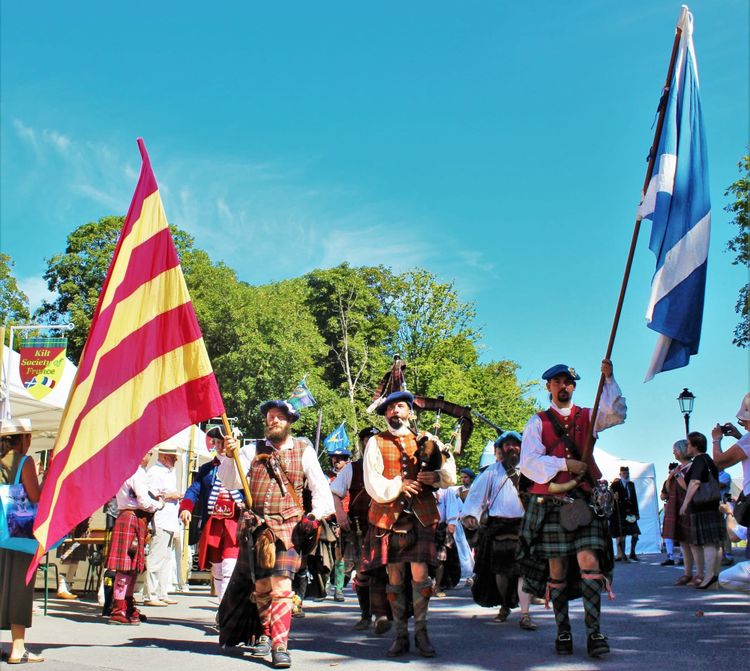 Pipers in historic Highland dress wave flags as they march through town.