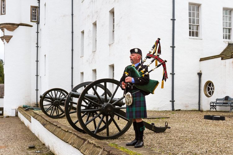 A bagpipe player stands next to an old cannon outside Blair Castle.