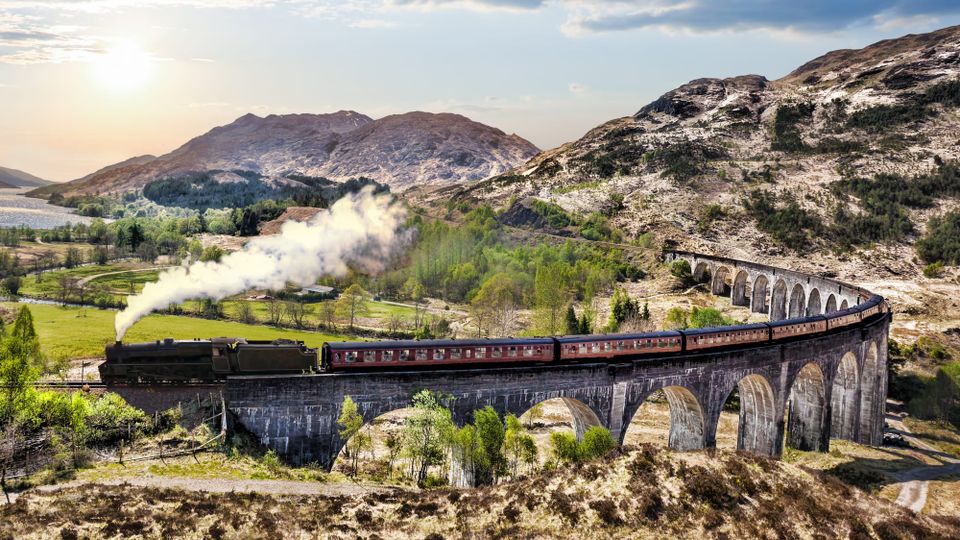 An aerial view of a steam train crossing the Glenfinnan Viaduct.