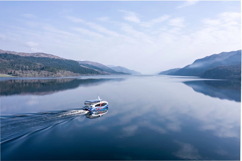 A boat sailing across Loch Ness on a bright day. The water is calm.