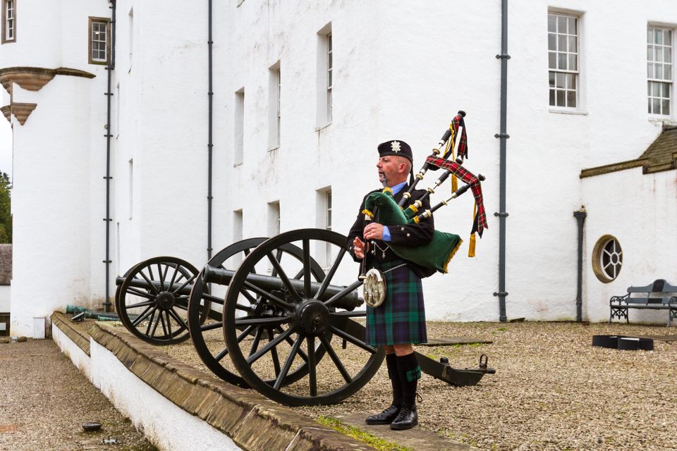 A bagpipe player stands next to an old cannon outside Blair Castle.