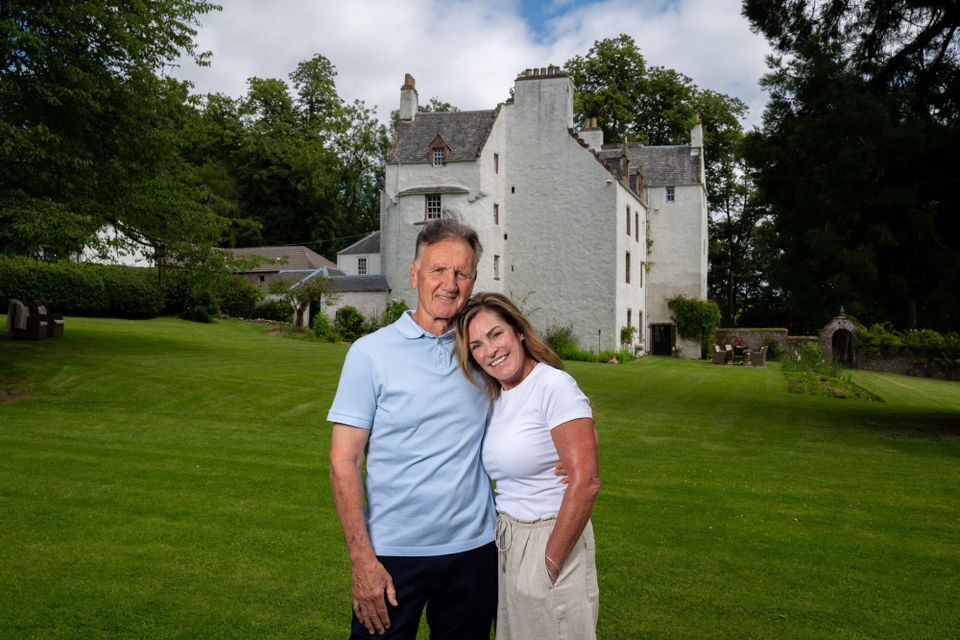 Margaret and David Hudson smile in the garden of Newton Castle, a white-painted castle.