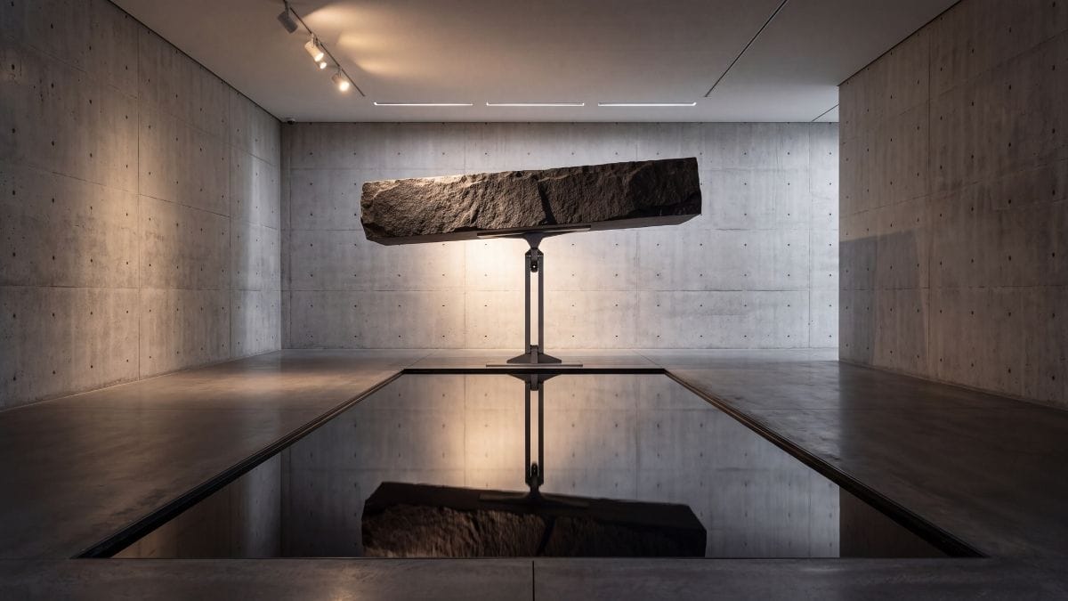 Minimalist granite and titanium counterbalance sculpture suspended over reflective dark water.