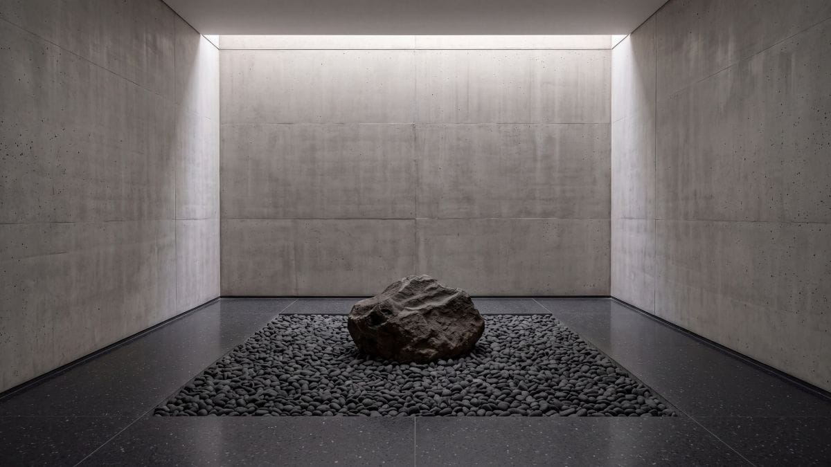 Minimalist Japanese-inspired stone meditation sanctuary with dark granite boulder and charcoal gravel.