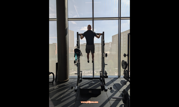Phil Jessé seemingly floats mid-air at the peak of a high pull-up at Deansgate Square, Manchester, showcasing mastery achieved through consistent effort.