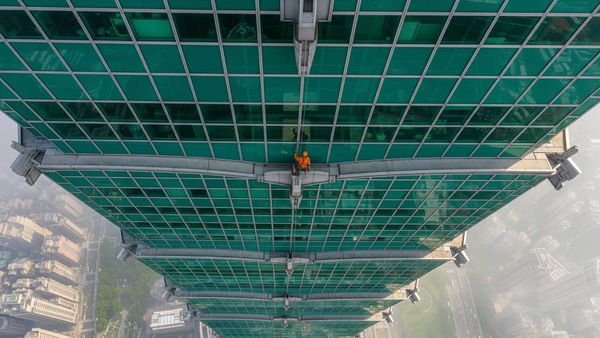 A climber free soloing the exterior glass and steel facade of the Taipei 101 skyscraper, high above the city.