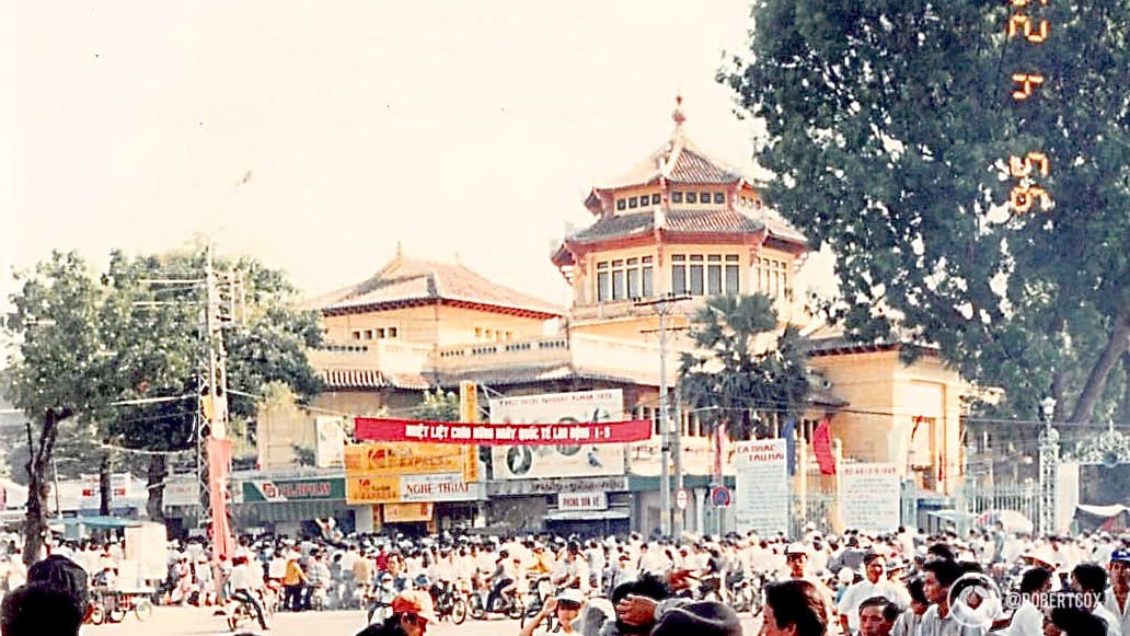 The prominent building in the background is the Vĩnh Nghiêm Pagoda, a well-known Buddhist temple in Ho Chi Minh City, recognizable by its distinctive seven-story tower with traditional Vietnamese architectural elements, such as the curved roof and ornate detailing. The pagoda, built in the 1960s, is a significant cultural and religious landmark in the city. (April 29, 1995)