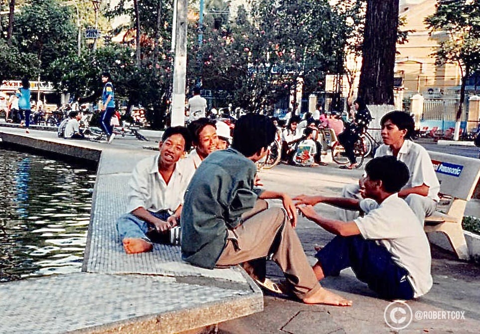 A group of people relaxing by the water, at the Nghiêm Pagoda in Ho Chi Minh City, Vietnam, near the pond and bridge area seen in the previous photo.