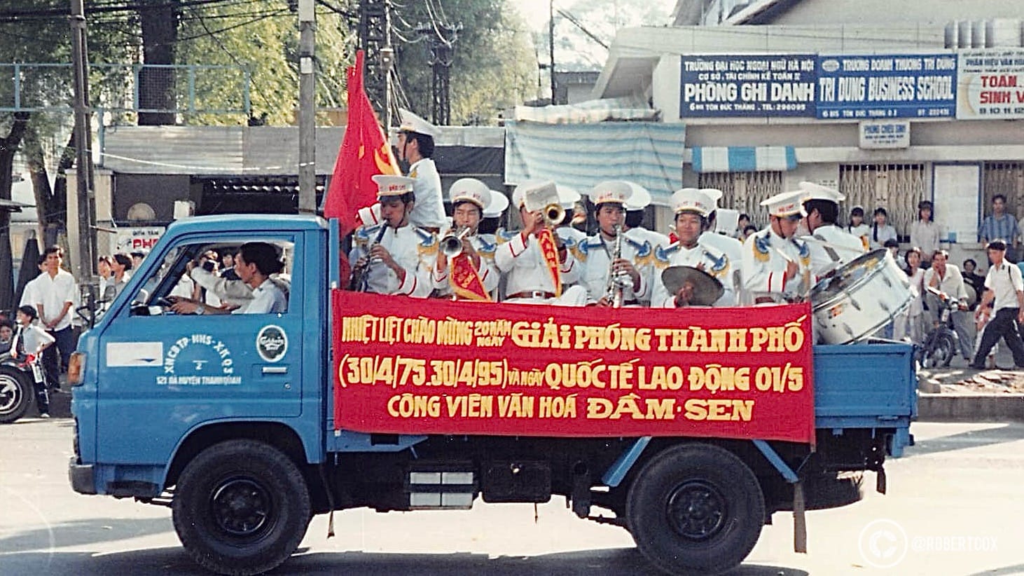 This banner indicates that the parade is celebrating two significant events: the 20th anniversary of Vietnam’s reunification, which occurred on April 30, 1975, marking the end of the Vietnam War, and International Labor Day, which is observed on May 1st. The text on the banner says, “PARADE CELEBRATING THE 20TH ANNIVERSARY OF REUNIFICATION (30/4/75 - 30/4/95) AND INTERNATIONAL LABOR DAY 01/5 CULTURAL WORKERS’ UNION” (April 30, 1995).