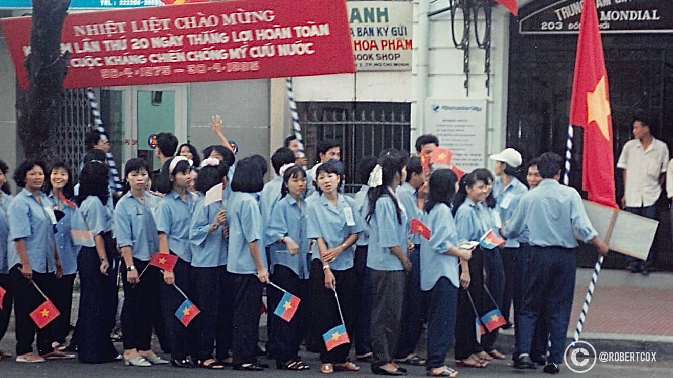 A group of young people in Ho Chi Minh City (Saigon), Vietnam, participating in the the 20th anniversary celebrations of Reunification Day. The red banner above reads, “Warmly Celebrate the 20th Anniversary of the Complete Victory of the Resistance War Against America for National Salvation, April 30, 1975 – April 30, 1995.” (April 29, 1995)