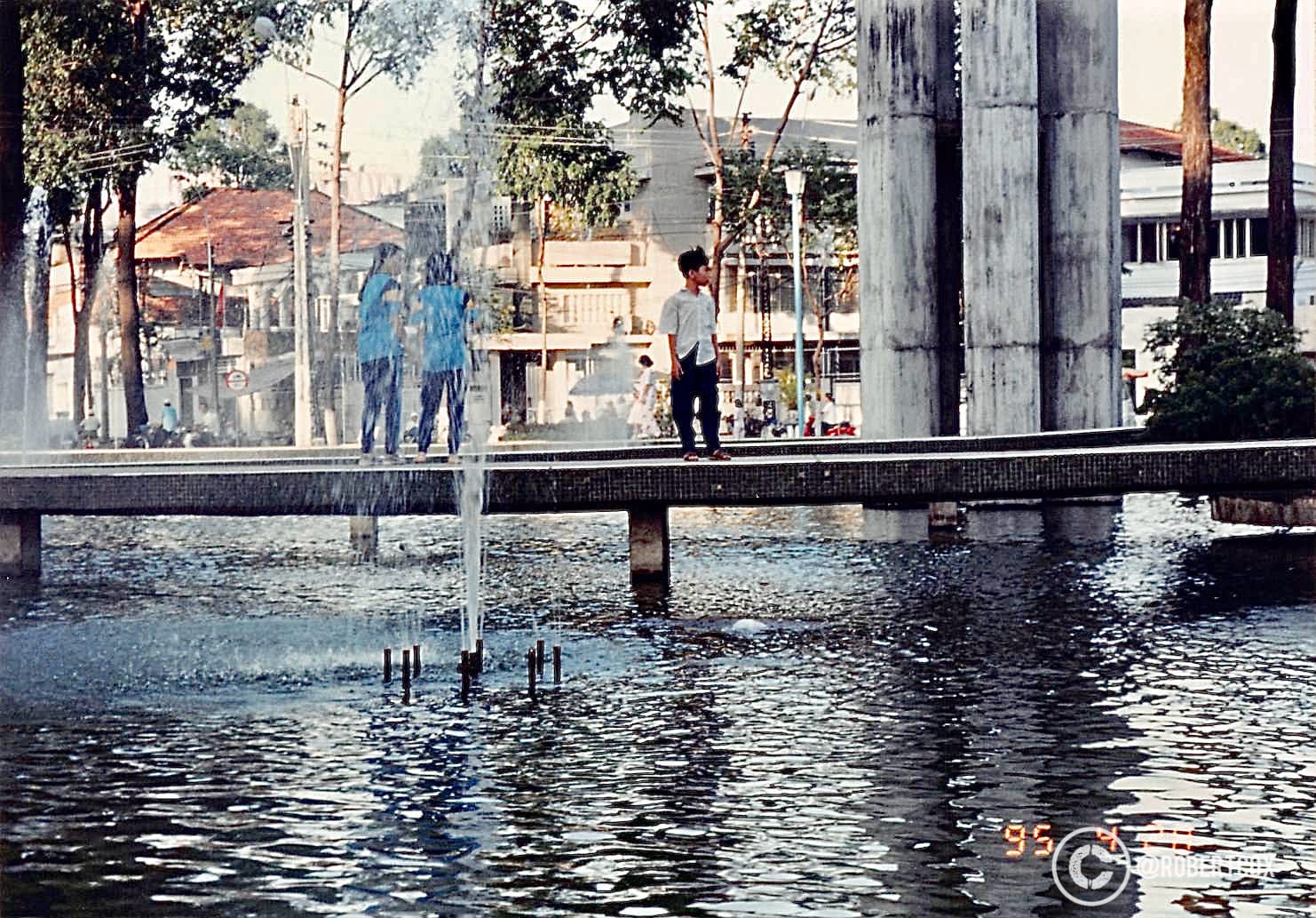 My minder-friend took me on Saturday, April 29, 1995, to see The Vĩnh Nghiêm Pagoda, also known as the Vĩnh Nghiêm Tower, in Ho Chi Minh City, Vietnam. The distinctive seven-story tower with its unique octagonal shape and the bridge over a pond with a fountain are characteristic features of this Buddhist temple. The pagoda, built in 1969, is a notable landmark in the city, known for its modernist architecture and cultural significance.