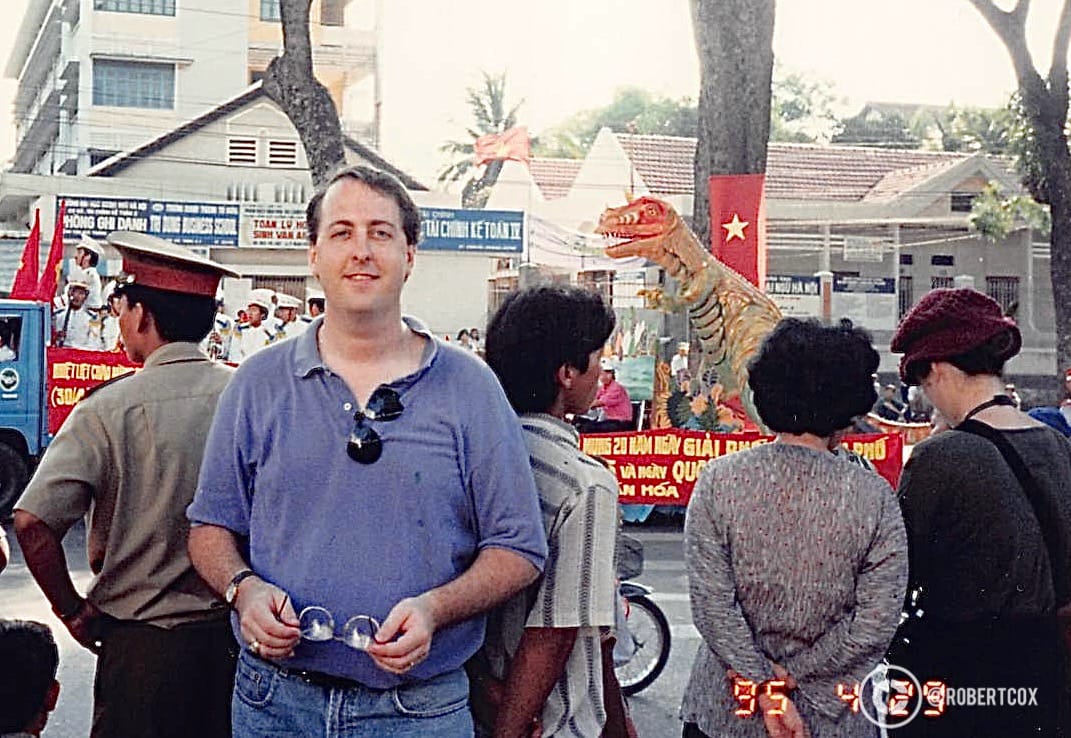 An image of me taken by the translator, at the “working area” for the parade celebrating the 20th anniversary of Vietnam’s reunification. There is a colorful dinosaur figure, maybe bring good luck and warding off evil spirits — or just because it looks cool. (April 30, 1995)