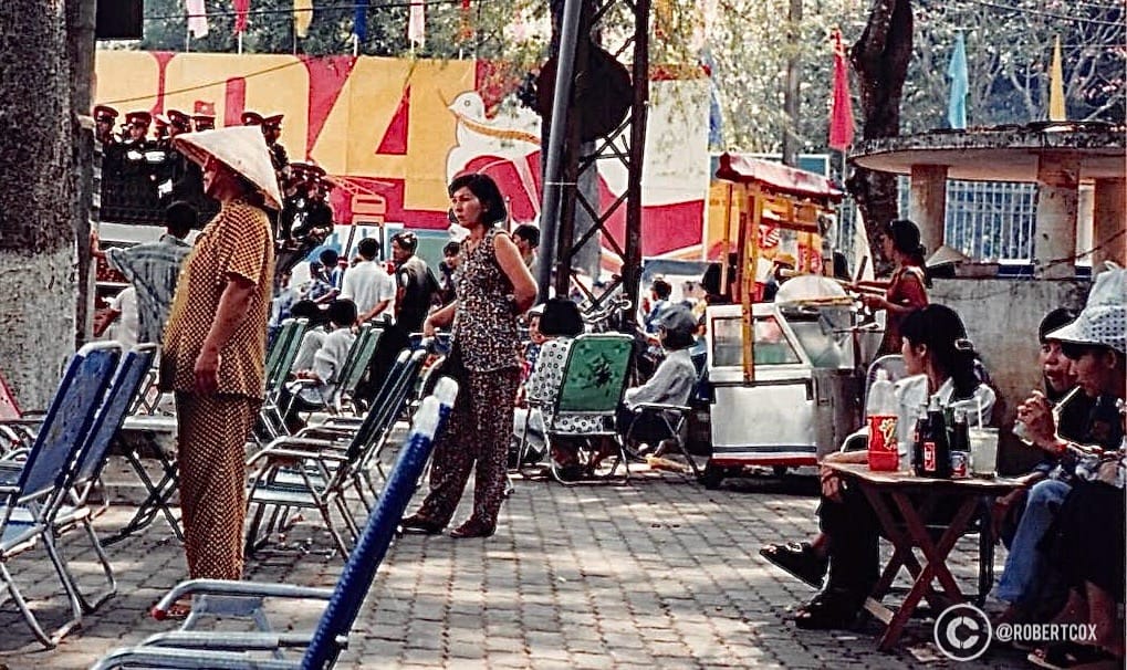 This photo, taken on April 30, 1995, captures a moment in Ho Chi Minh City (Saigon), Vietnam, shortly before the start of a parade celebrating the 20th anniversary of Reunification Day. The scene shows people gathered in a public space, waiting for the parade to begin, reflecting the festive atmosphere of this significant national holiday. This is where a lady tried to sell me a Coke for ten-times the normal price.