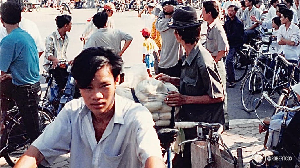 A street scene in front of the famous seven-story pagoda, which is the Vĩnh Nghiêm Pagoda. The image shows a group of locals on motorbikes and bicycles, reflecting the everyday life of Saigon during the 20th anniversary celebrations of Reunification Day. (April 29, 1995)