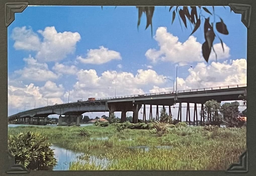 This image is a postcard depicting the Saigon Bridge (Cầu Sài Gòn) spanning the Saigon River in Ho Chi Minh City, Vietnam. It was originally built in 1961 as part of infrastructure development during the South Vietnamese regime, with support from the United States as part of its military and economic aid to South Vietnam. The bridge was strategically important, connecting Saigon to the Bien Hoa Highway and facilitating access to military bases and industrial areas in the east, including the port of Cat Lai. During the Vietnam War, it was a key transportation route, often targeted by the Viet Cong due to its significance. After the fall of Saigon in 1975, the bridge continued to serve as a vital link under the communist government, supporting the city’s economic activities as Vietnam began its Đổi Mới reforms in 1986. (April 30, 1995)