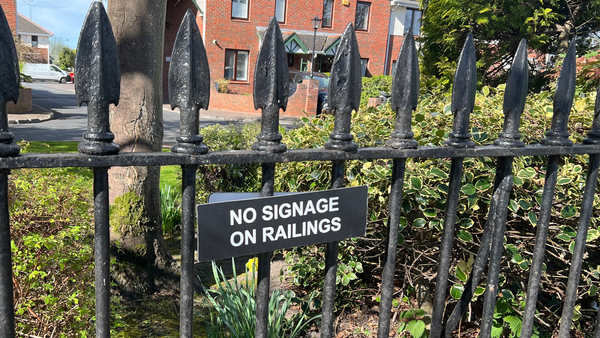 A sign hung on a railing in front of a house reading “No signage on railings”.