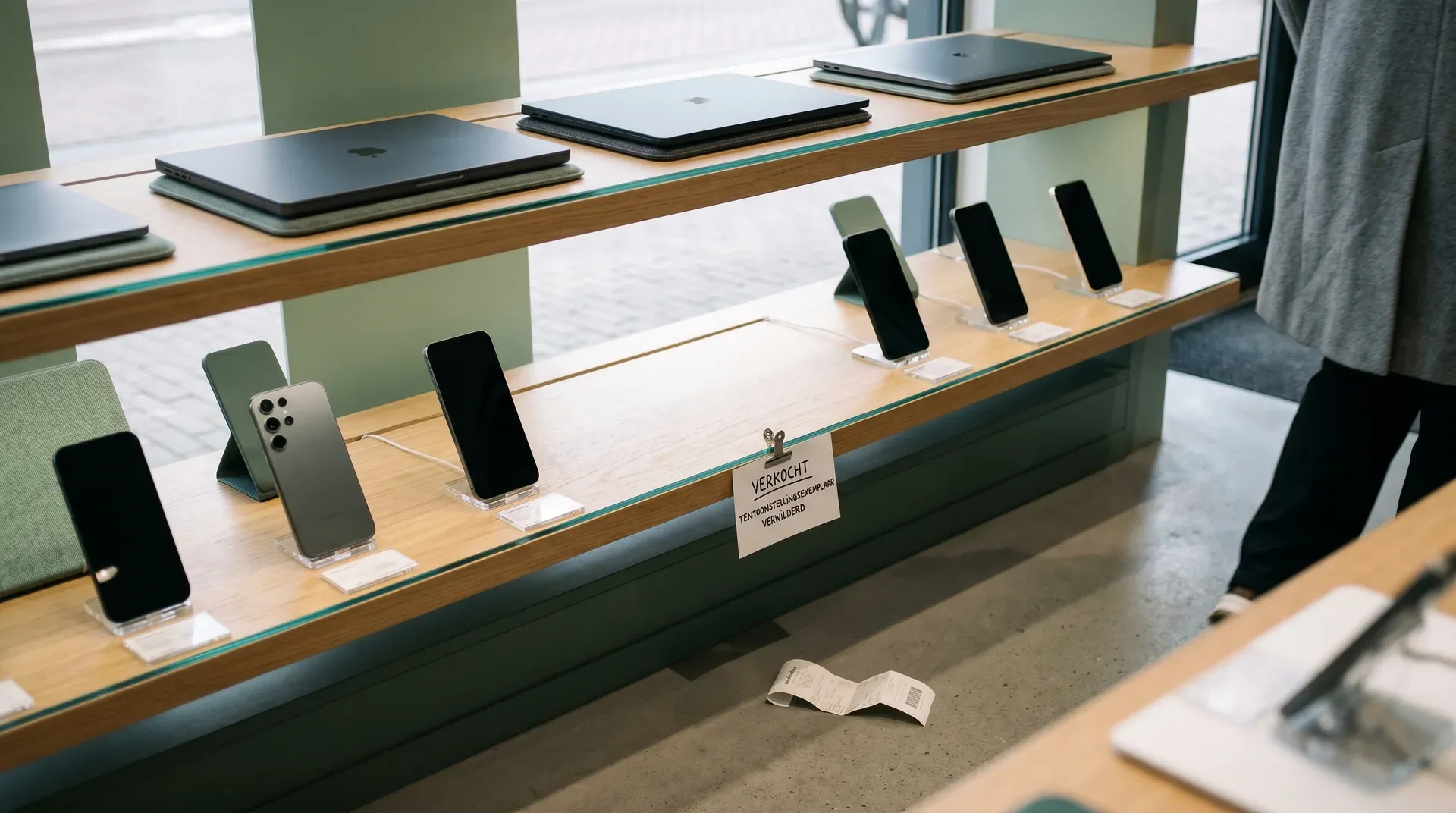 Winkeluitstalling met Apple laptops en smartphones in houten vitrinekast met groene achtergrond