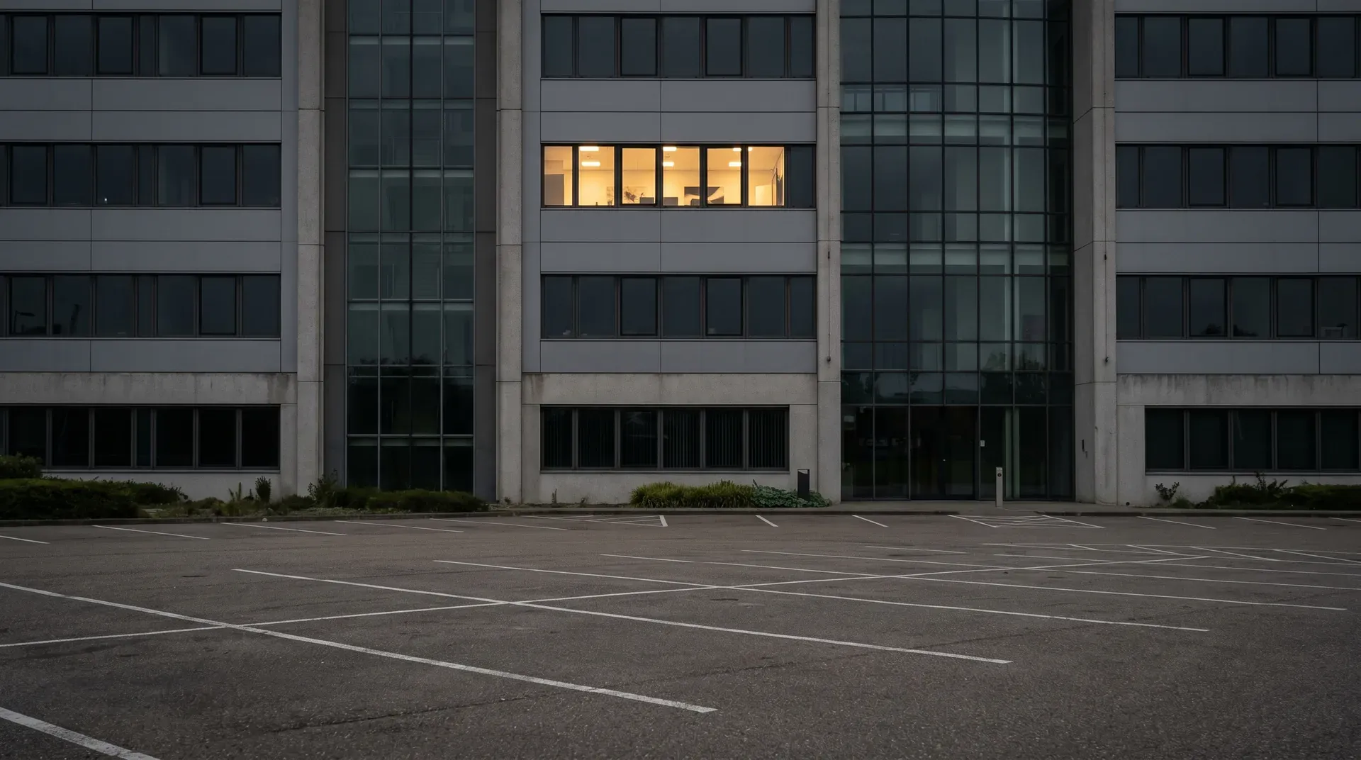 Lege parkeerplaats voor modern kantoorgebouw met verlichte ramen in schemering
