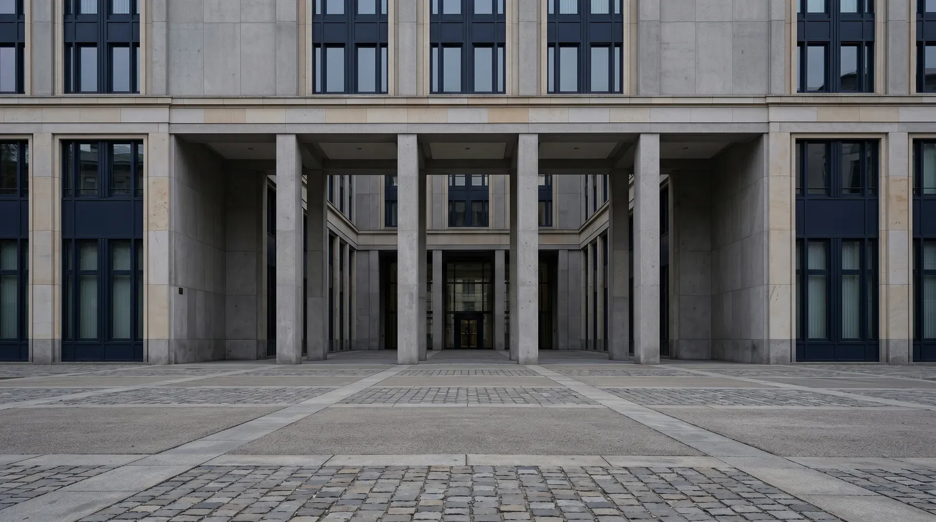 Symmetrische voorgevel van modern kantoorgebouw met stenen kolommen en glazen deuren.