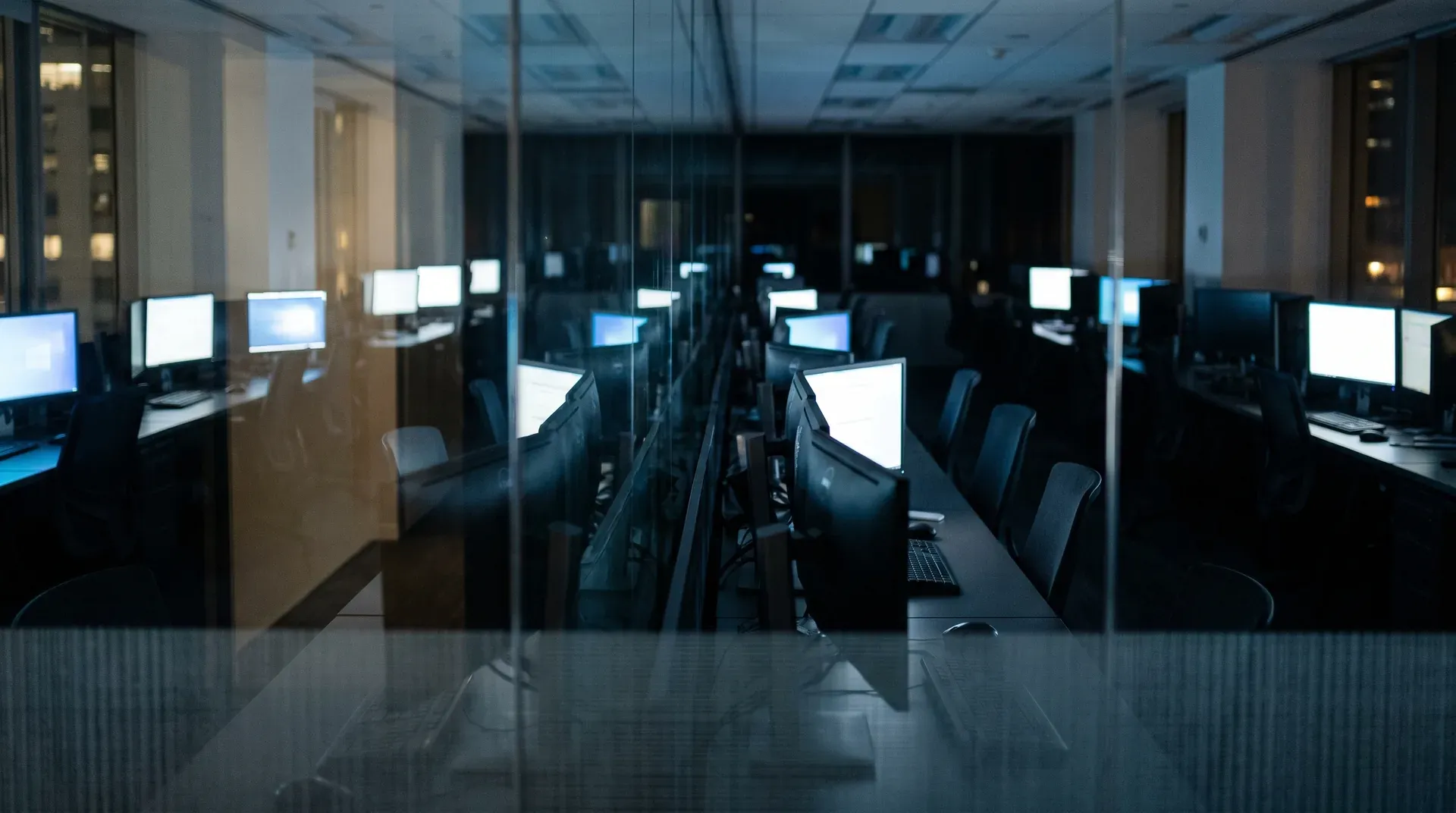 Moderne kantoorruimte met computerworkstations en verlichte schermen in donkere avondsfeer.