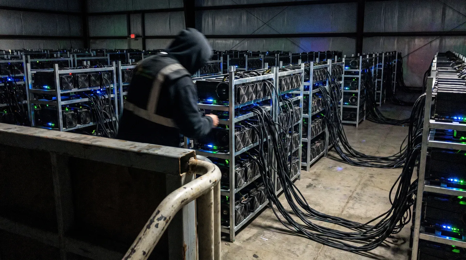 Technicus loopt tussen rijen mining-computers met blauwe LED's in industriële opslagruimte