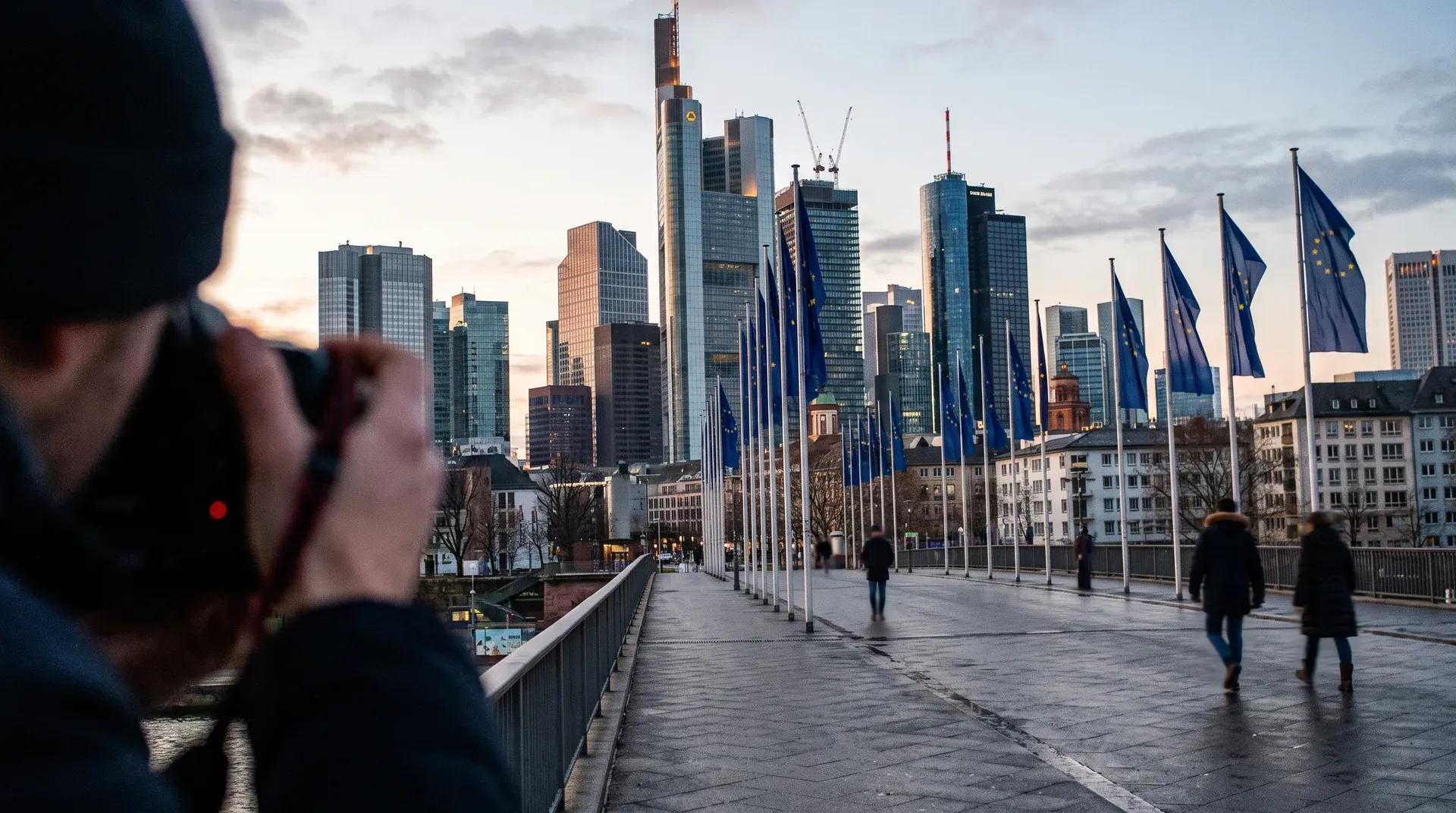 Skyline van Frankfurt met wolkenkrabbers, EU-vlaggen op pleintje, persoon fotografeert voorgrond