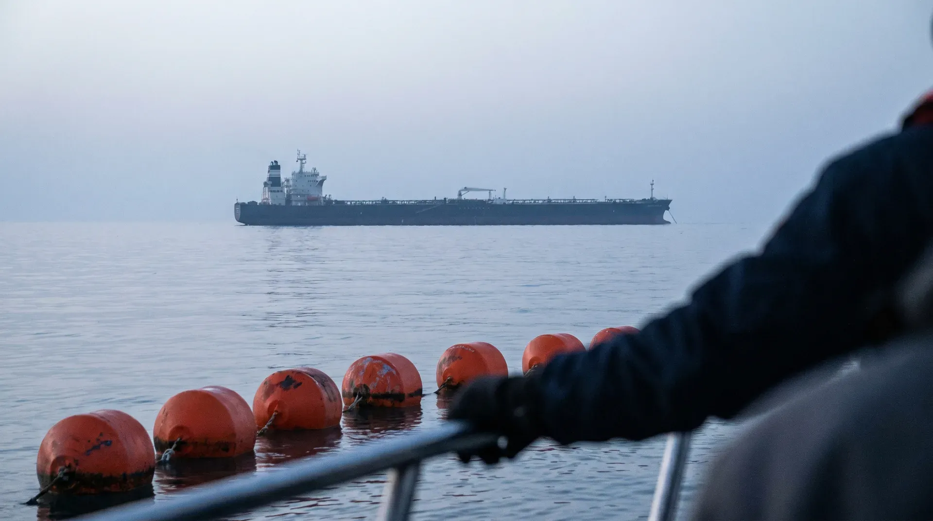 Tanker op open zee gezien vanaf schip met rode boeien en zwart touw op voorgrond