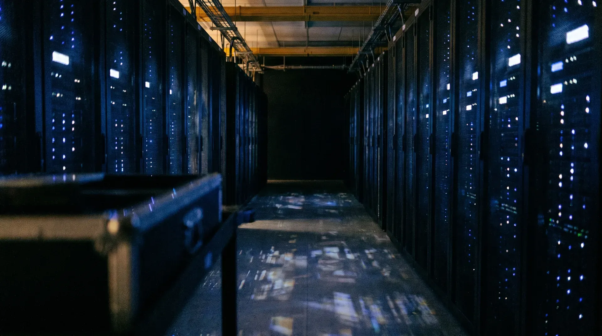 Datacentrum-gang met serverrekken verlicht door blauwe ledlampjes en gele overhead-kranen