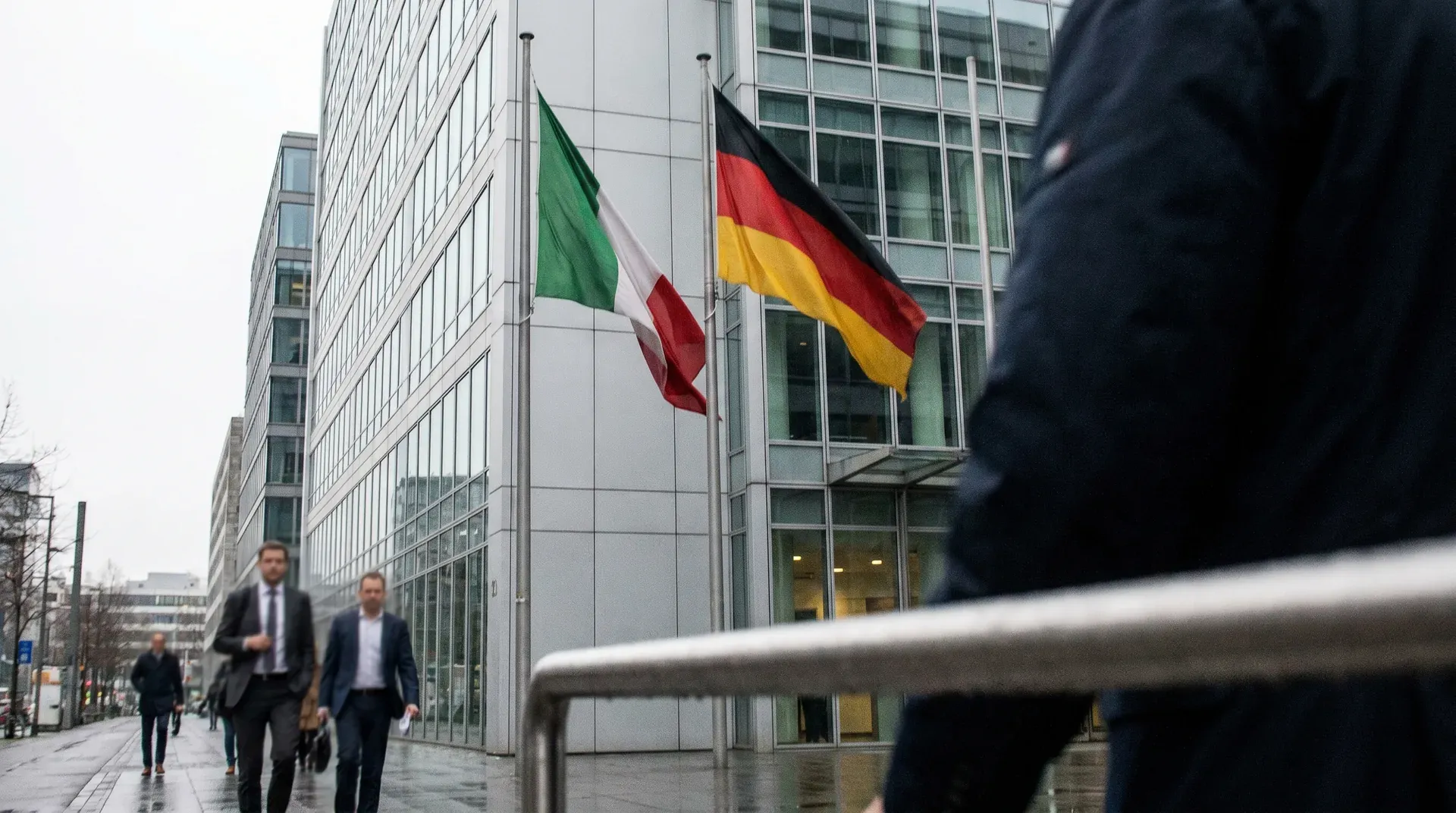 Duitse en Italiaanse vlaggen wapperen voor moderne kantoorgebouwen met zakenlieden op straat.