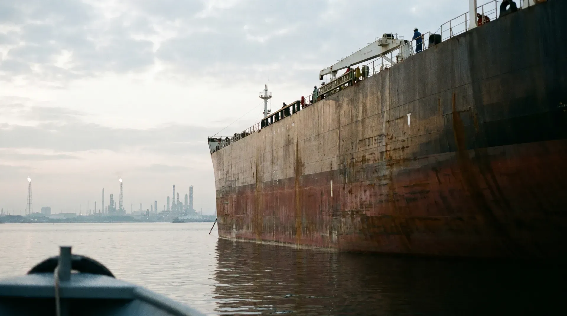 Grote olietanker aangelegd in haven met industriële raffinaderij op achtergrond