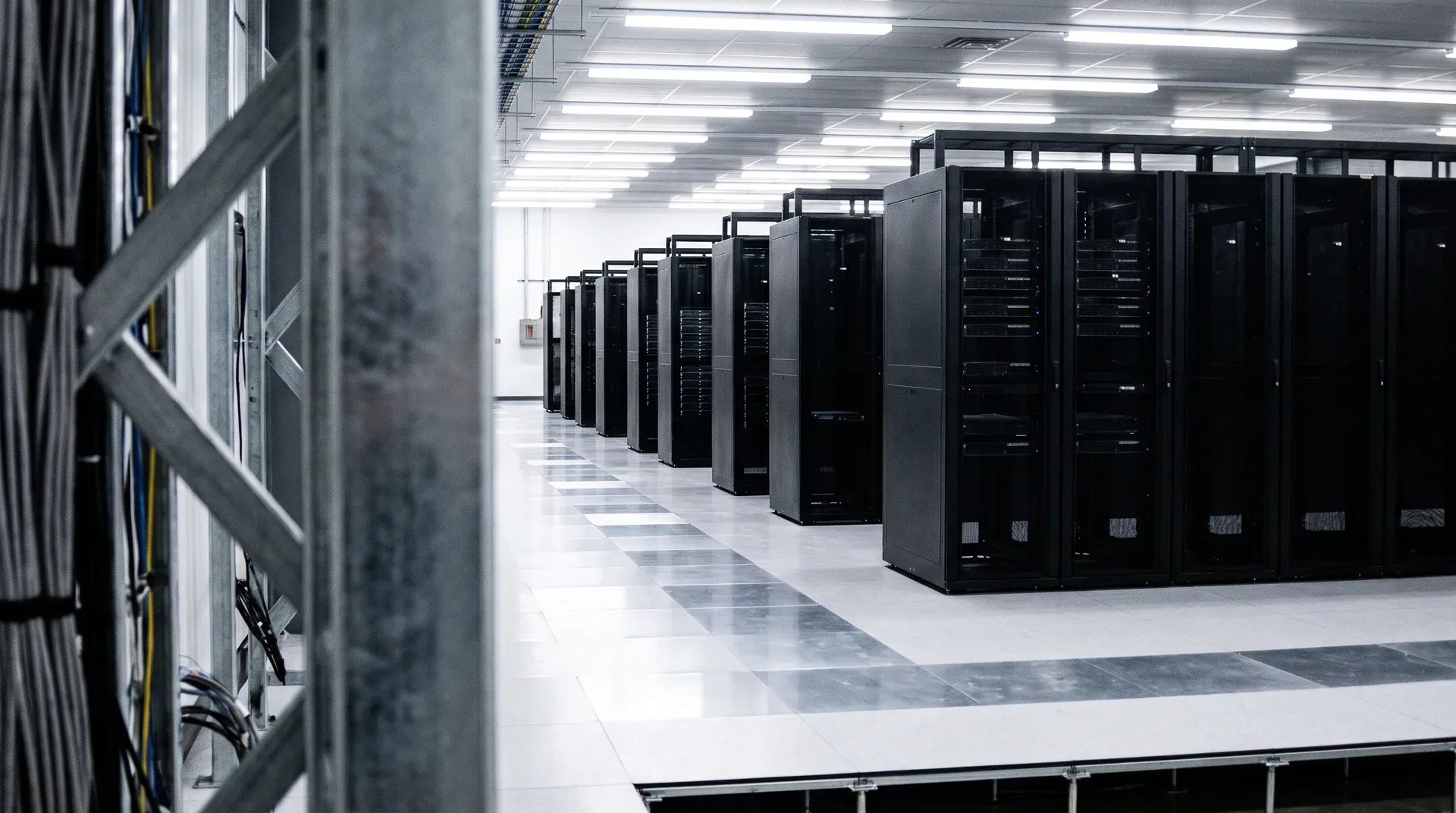 Rij zwarte serverkasten in moderne datacentrum met fluorescente verlichting en wit vloerwerk.