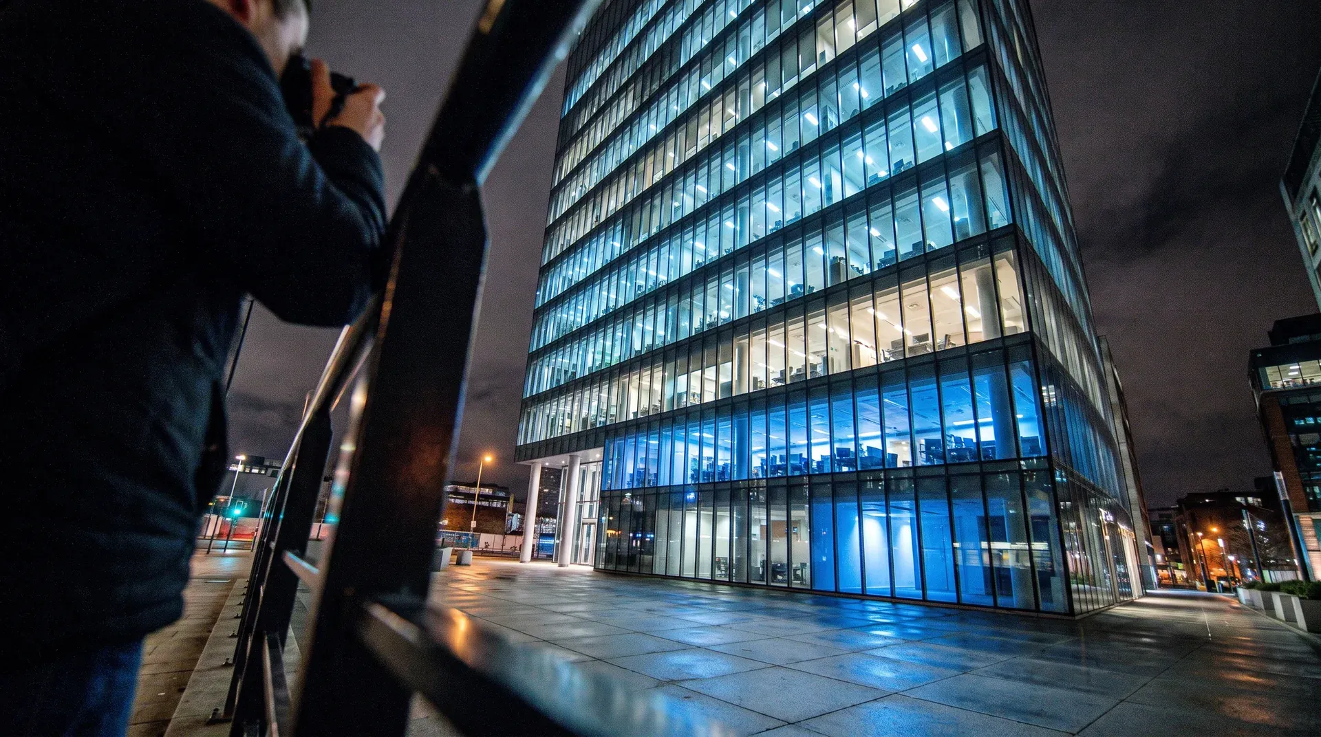 Modern glazen kantoorgebouw 's nachts verlicht met blauwe lichten, persoon op voorgrond