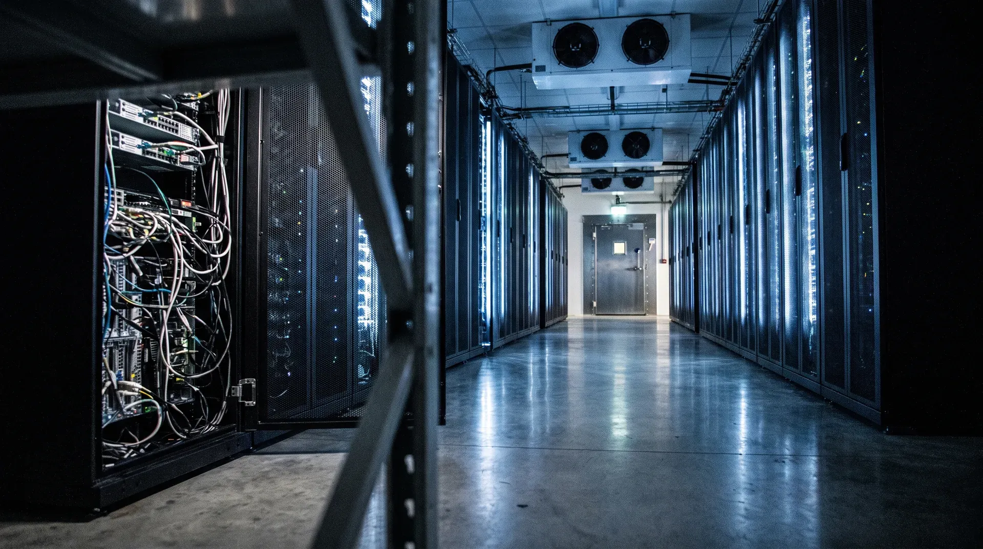 Lange gang in moderne serverhal met zwarte racks en blauwe LED-verlichting aan zijkanten, koelunits aan plafond