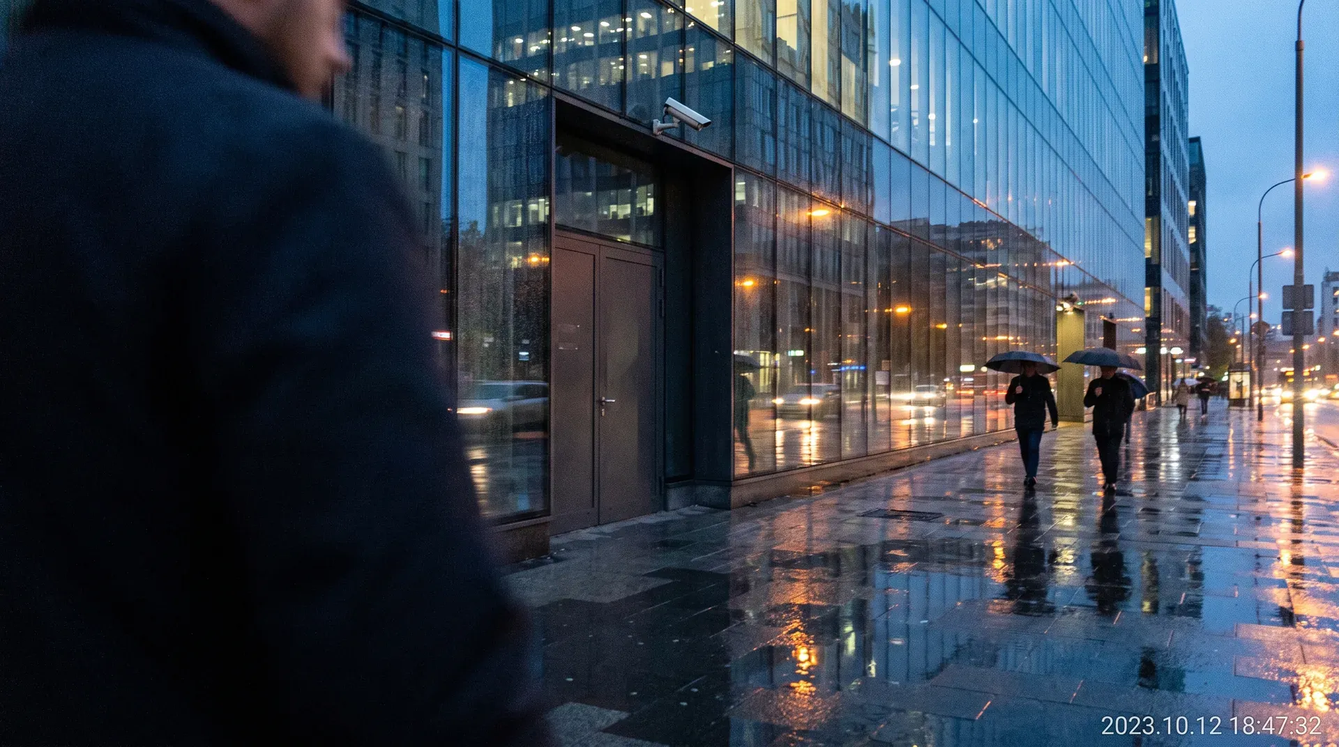 Regenachtig stadsstraat bij schemering met glas kantoorgebouwen en voetgangers met paraplu's