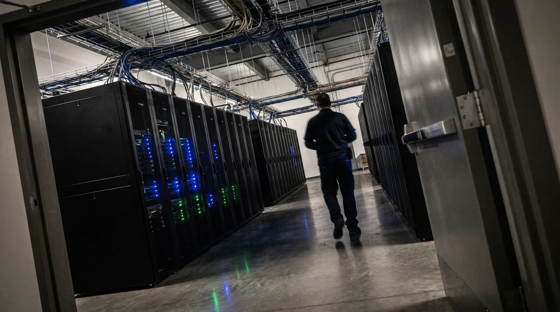 Technicus loopt door serverhal met zwarte racks en blauwe/groene indicator-leds