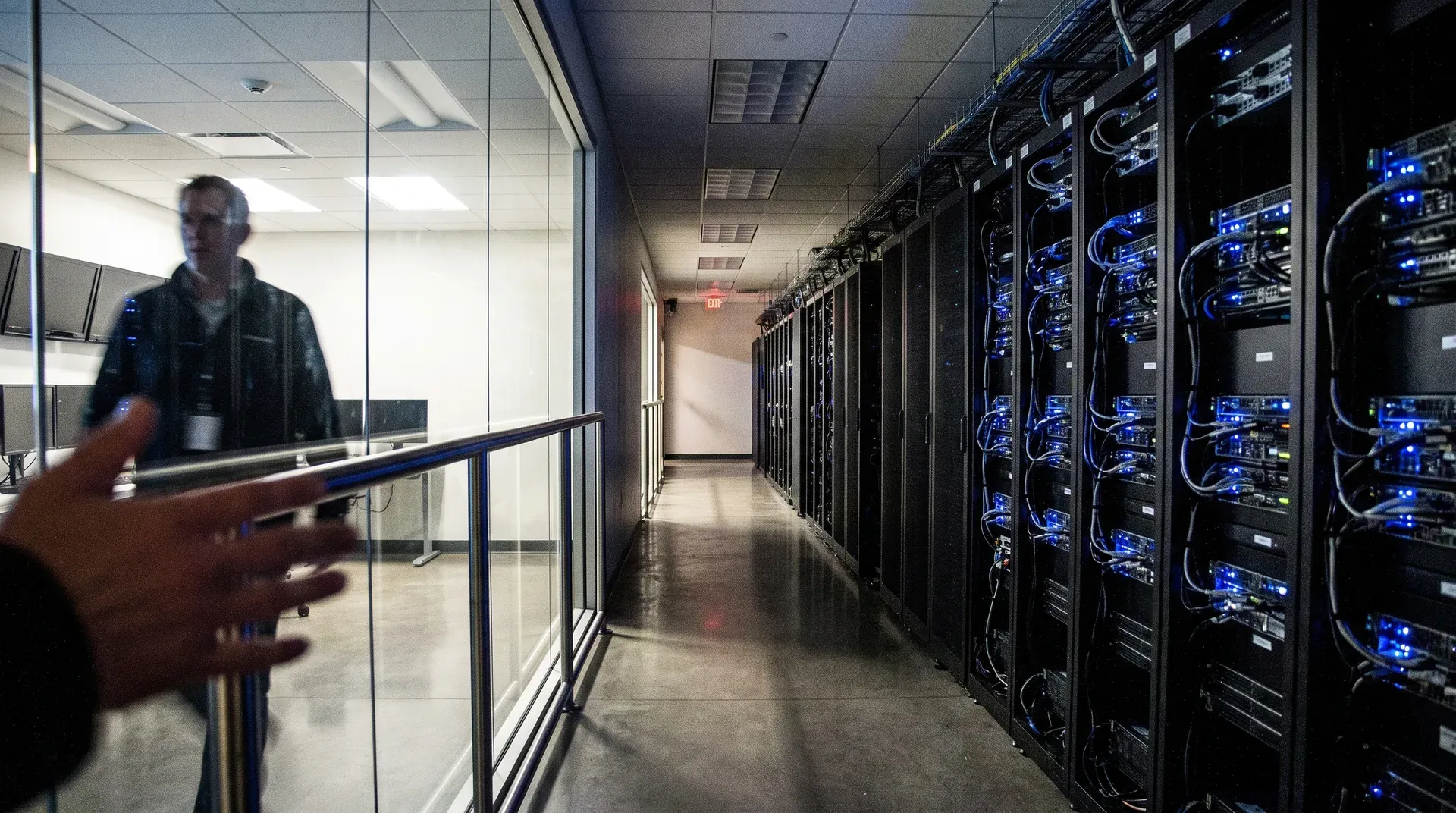 Datacentrum gang met server racks en blauwe LED-verlichting, persoon achter glas aan het werk