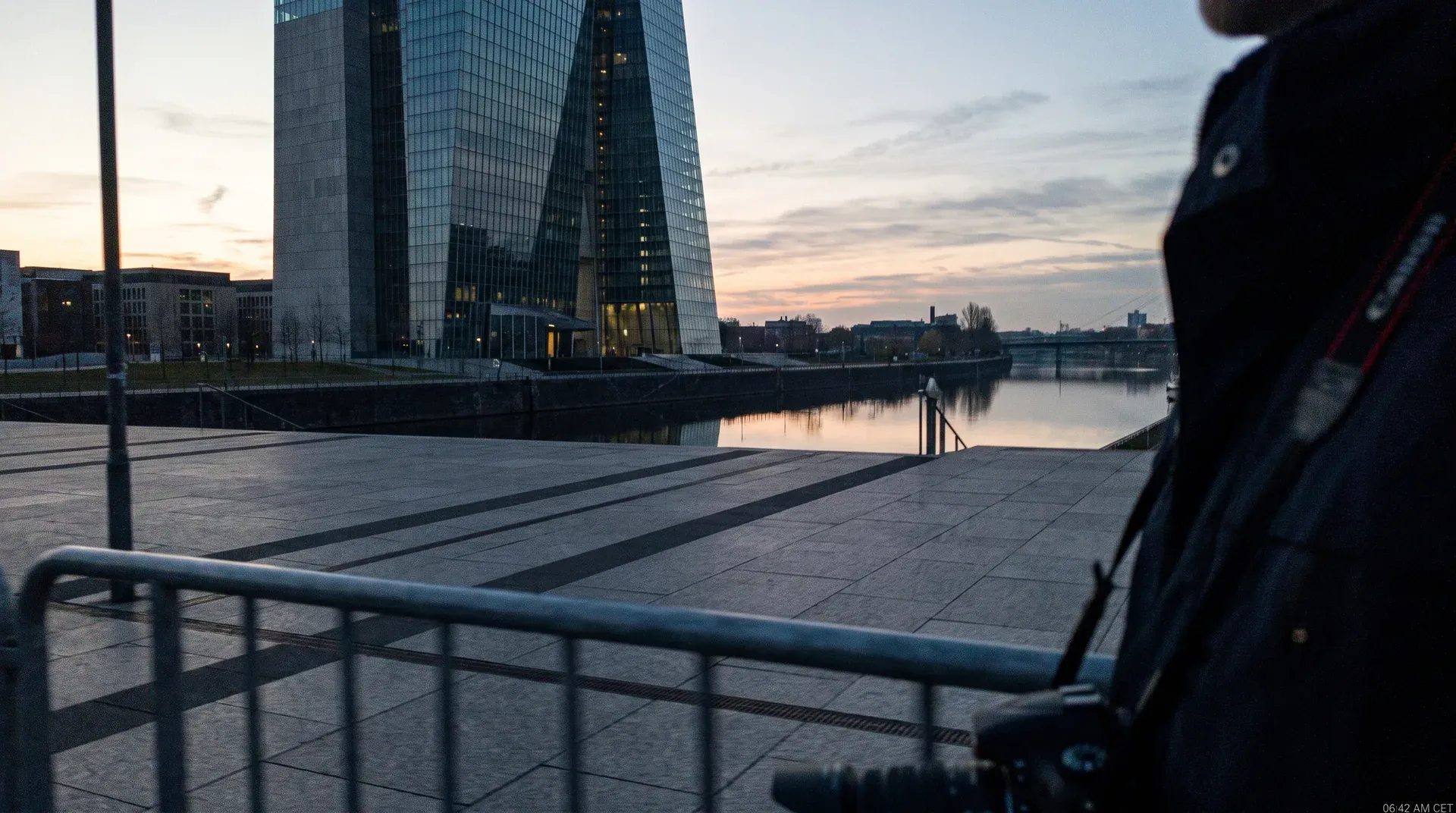 Modern glazen kantoorgebouw aan waterfront bij zonsopgang, spiegeling in stil water, stedelijke skyline op achtergrond