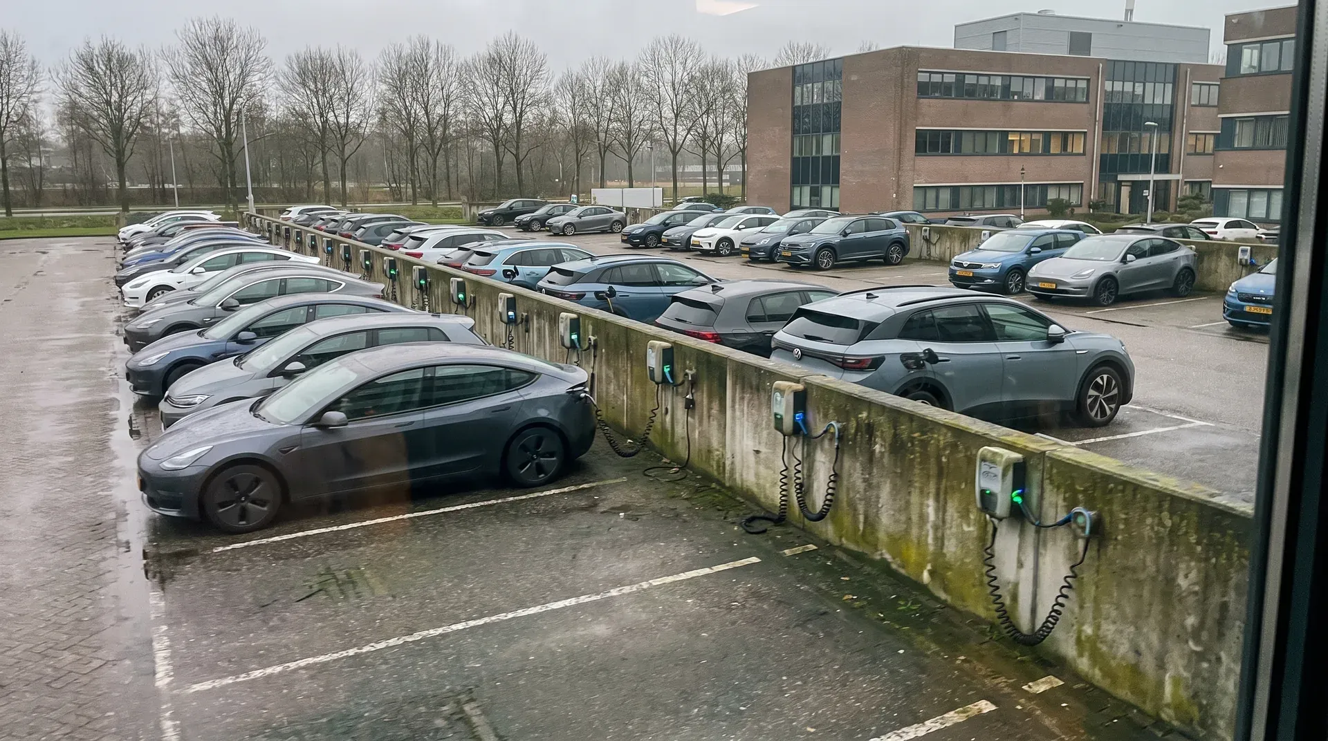 Rij elektrische auto's aan laadstations op parkeerterrein naast kantoorgebouw
