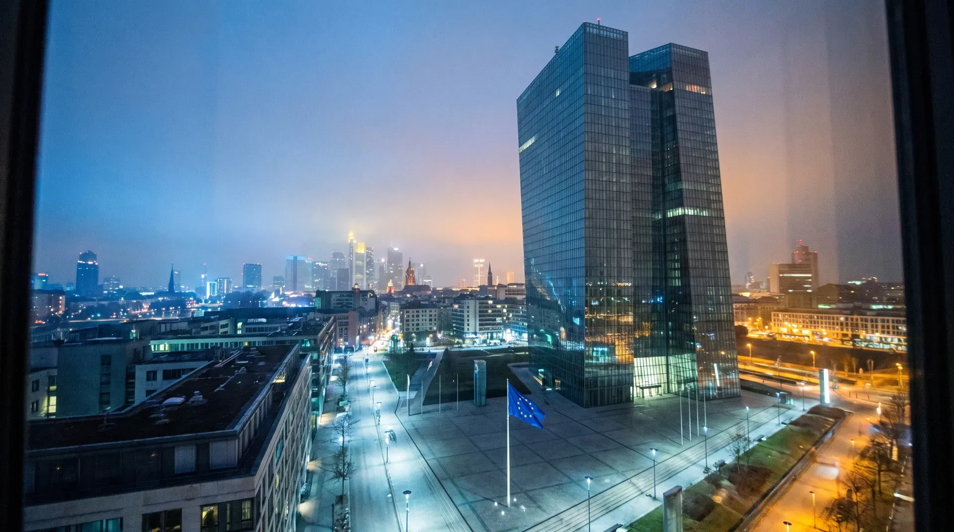 Skyline van Frankfurt bij schemering met moderne kantoorgebouwen, EU-vlag op plein, avondlichten