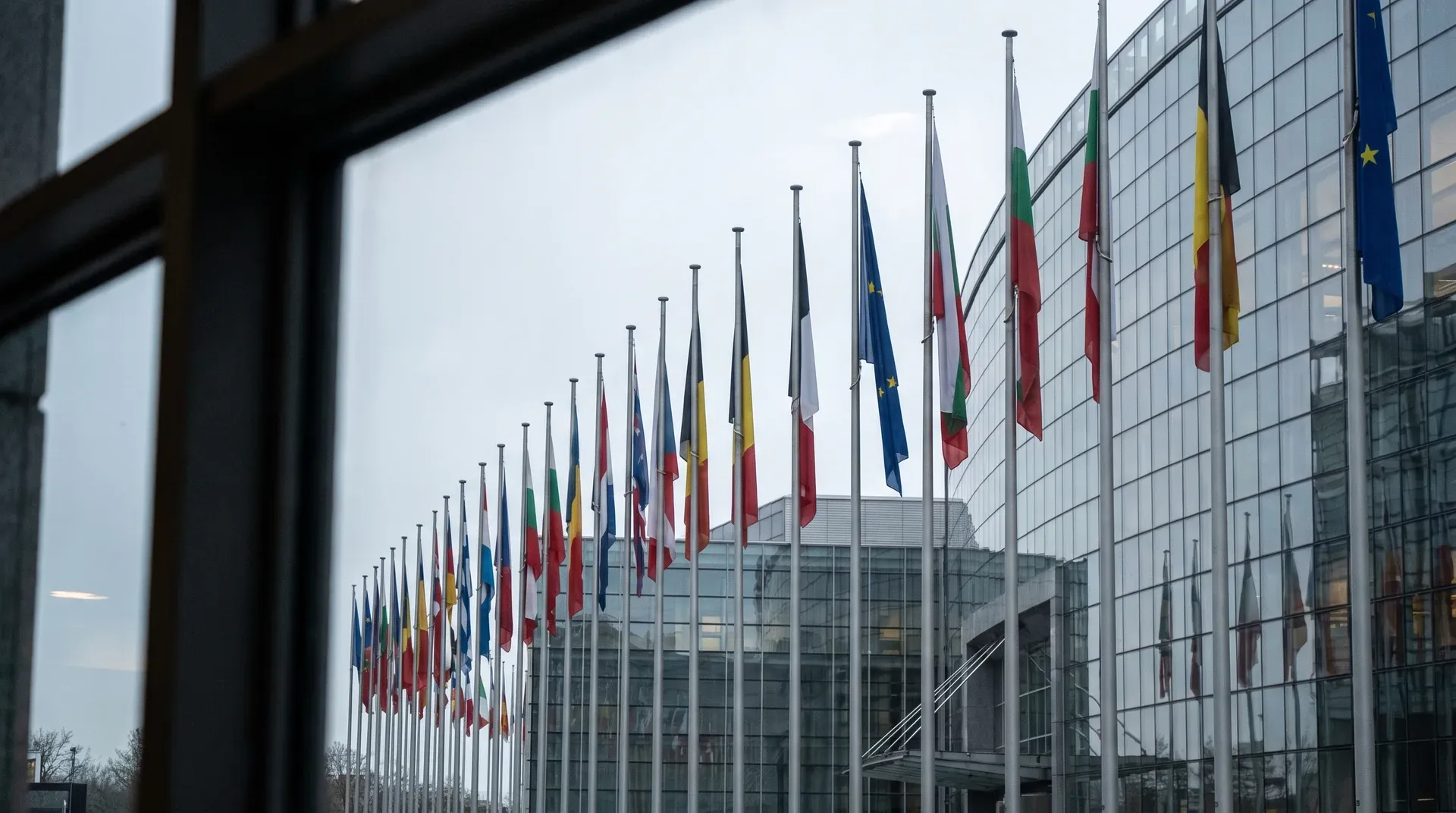 Rij vlaggen van EU-lidstaten op masten voor modern glasgebouw, symboliserend Europese instellingen